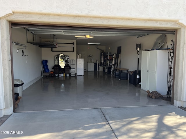 garage featuring washer and clothes dryer, gas water heater, and freestanding refrigerator