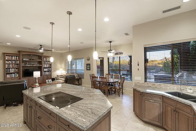 kitchen featuring light stone countertops, pendant lighting, a kitchen island, black electric stovetop, and sink