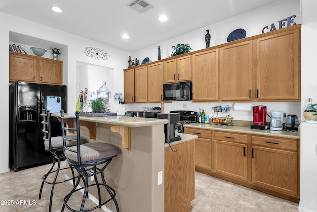 kitchen featuring a kitchen bar, light tile patterned floors, a kitchen island, and black appliances