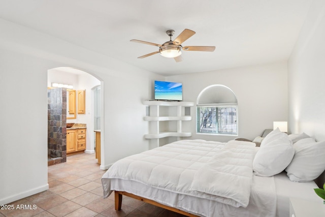 7734 E Rose Ln, Scottsdale, AZ 85250 - bedroom featuring arched walkways, baseboards, ceiling fan, connected bathroom, and light tile patterned floors