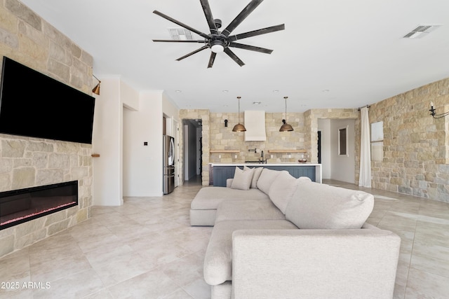 living room with sink, a stone fireplace, and ceiling fan