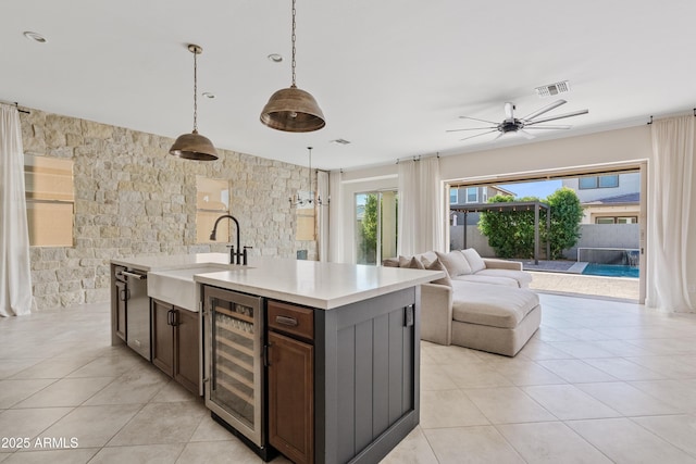 kitchen featuring sink, hanging light fixtures, wine cooler, dark brown cabinetry, and an island with sink