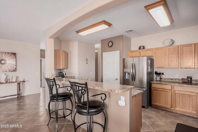 kitchen with tile patterned flooring, light brown cabinets, stainless steel fridge with ice dispenser, a breakfast bar area, and a peninsula