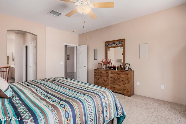 carpeted bedroom featuring a ceiling fan, visible vents, and arched walkways