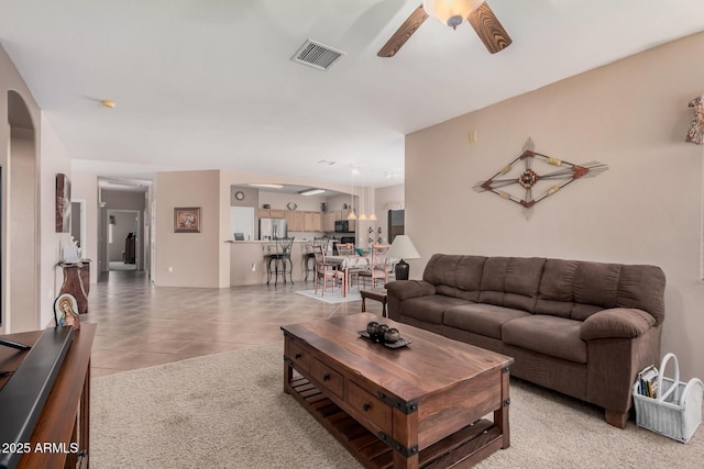 living area featuring light tile patterned floors, a ceiling fan, visible vents, and arched walkways