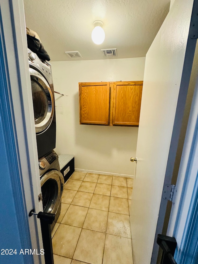 laundry area with light tile patterned flooring, cabinets, a textured ceiling, and stacked washer and clothes dryer