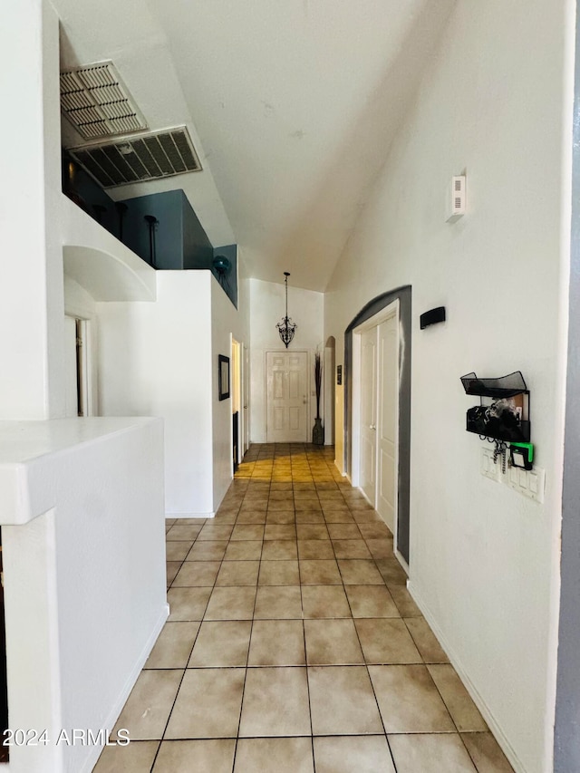 corridor featuring tile patterned floors, high vaulted ceiling, and an inviting chandelier