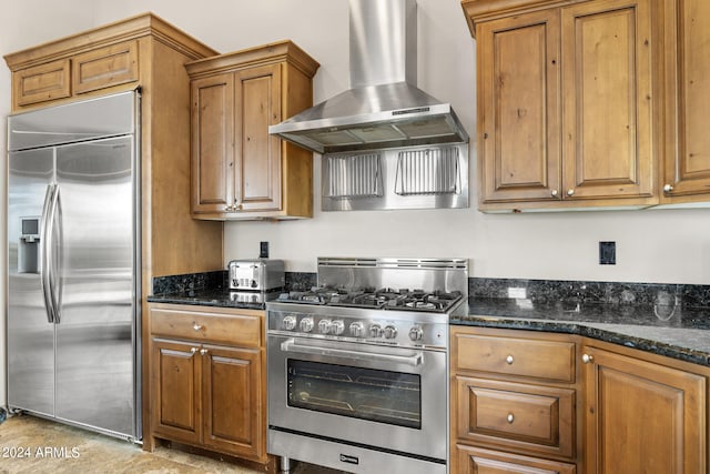 kitchen featuring dark stone countertops, high end appliances, and wall chimney range hood