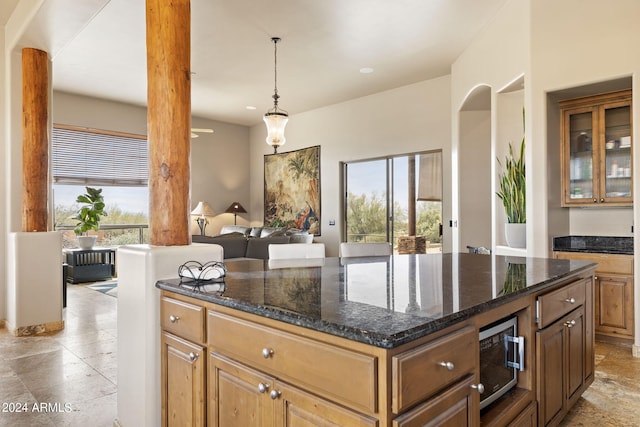 kitchen featuring hanging light fixtures, dark stone countertops, a center island, and a healthy amount of sunlight