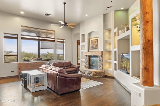 living room with ceiling fan, a stone fireplace, dark hardwood / wood-style flooring, and built in shelves