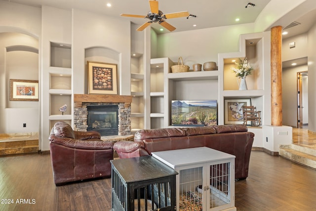 living room featuring dark wood-type flooring, ceiling fan, built in shelves, and a stone fireplace