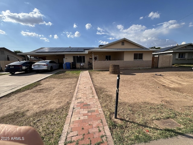 single story home with concrete driveway, solar panels, brick siding, a carport, and a porch