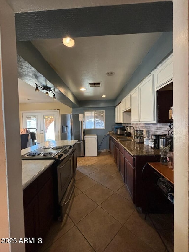 kitchen with electric range oven, stainless steel fridge with ice dispenser, white cabinetry, dark tile patterned floors, and a sink