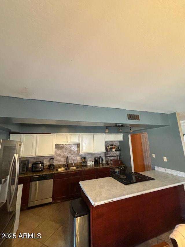 kitchen featuring appliances with stainless steel finishes, light tile patterned floors, decorative backsplash, white cabinets, and a sink