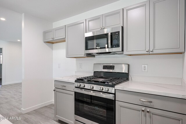 kitchen with light stone counters, appliances with stainless steel finishes, gray cabinetry, and light wood-type flooring