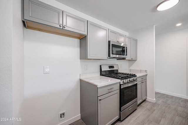 kitchen featuring appliances with stainless steel finishes, gray cabinets, light hardwood / wood-style floors, and light stone counters