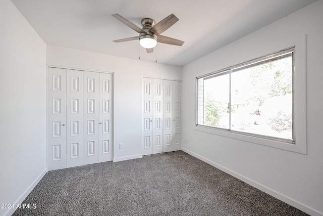 unfurnished bedroom with two closets, ceiling fan, and dark colored carpet