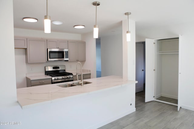 kitchen with decorative light fixtures, light stone counters, appliances with stainless steel finishes, and light wood-type flooring