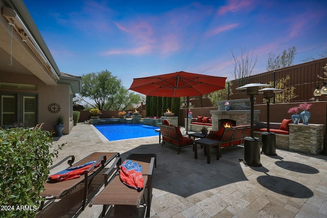 pool at dusk with a patio and an outdoor stone fireplace