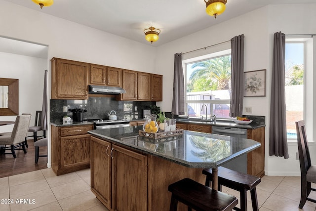 kitchen with light tile patterned floors, brown cabinets, a sink, appliances with stainless steel finishes, and backsplash