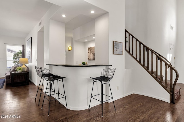 kitchen with dark wood finished floors, visible vents, a breakfast bar, and baseboards