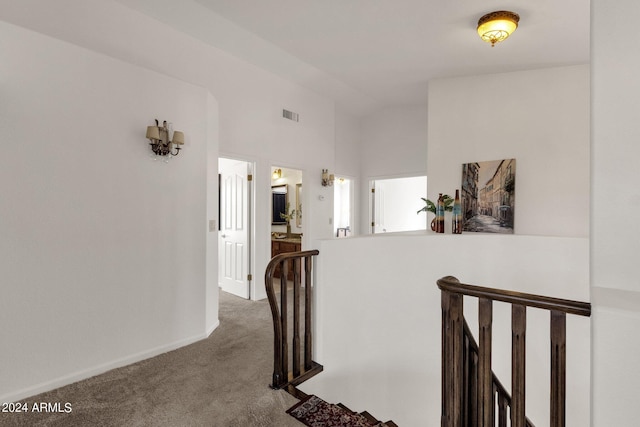 hallway with vaulted ceiling, an upstairs landing, carpet flooring, baseboards, and visible vents