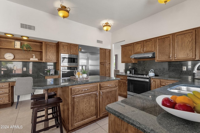 kitchen with a sink, under cabinet range hood, built in appliances, light tile patterned floors, and visible vents