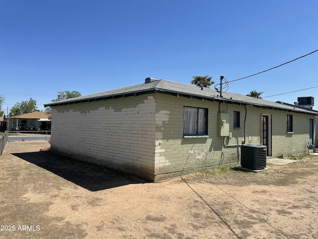 view of property exterior featuring central AC, brick siding, fence, and roof with shingles