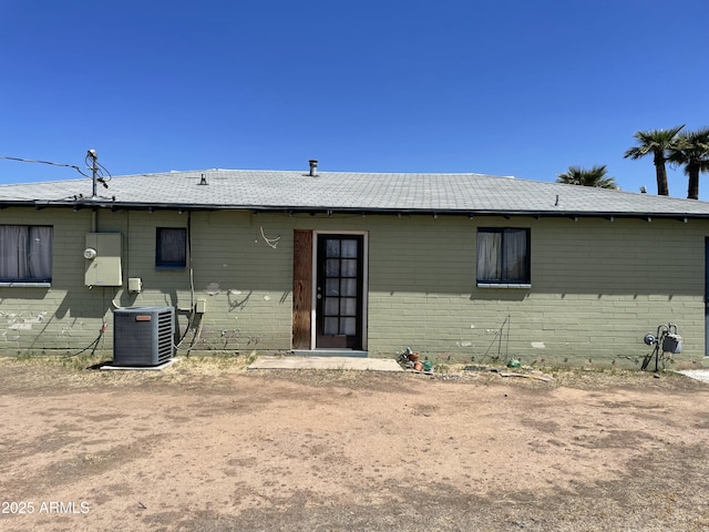 rear view of property featuring brick siding, central AC unit, and roof with shingles