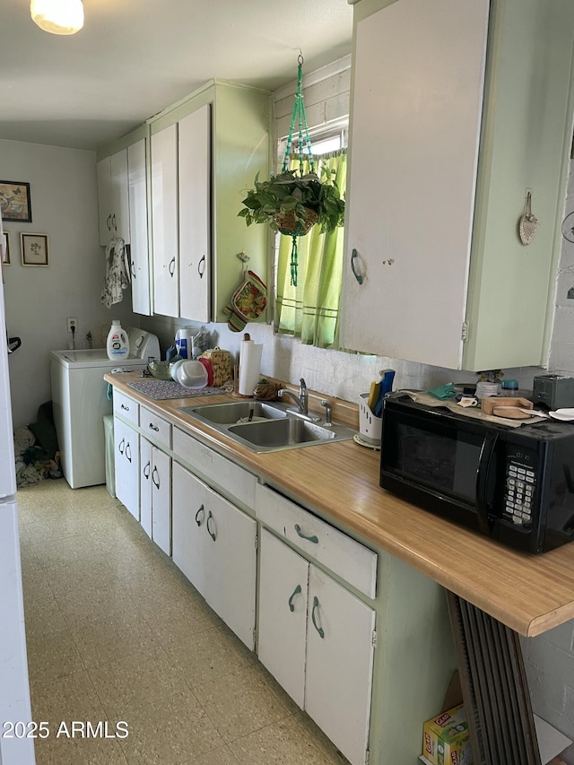 kitchen with black microwave, a sink, light countertops, white cabinets, and light flooring