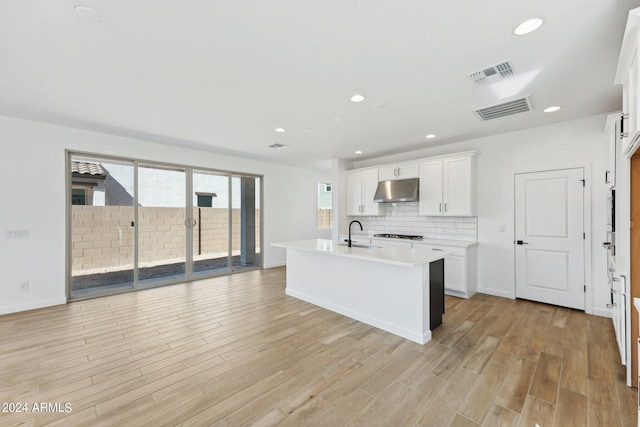 kitchen with tasteful backsplash, a kitchen island with sink, white cabinets, and light wood-type flooring