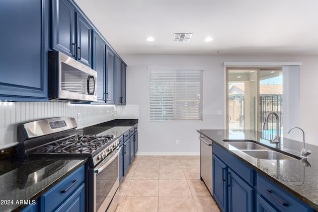 kitchen featuring dark stone countertops, appliances with stainless steel finishes, blue cabinetry, and sink