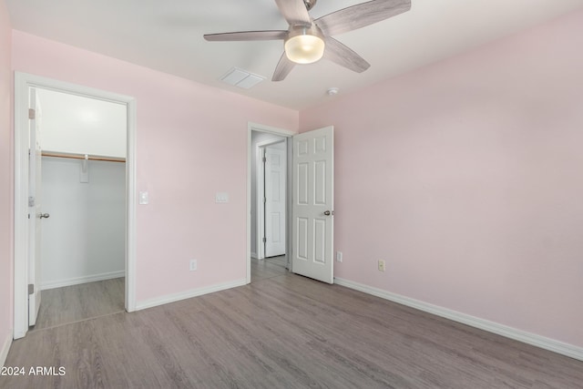 unfurnished bedroom featuring ceiling fan, a spacious closet, a closet, and light hardwood / wood-style flooring