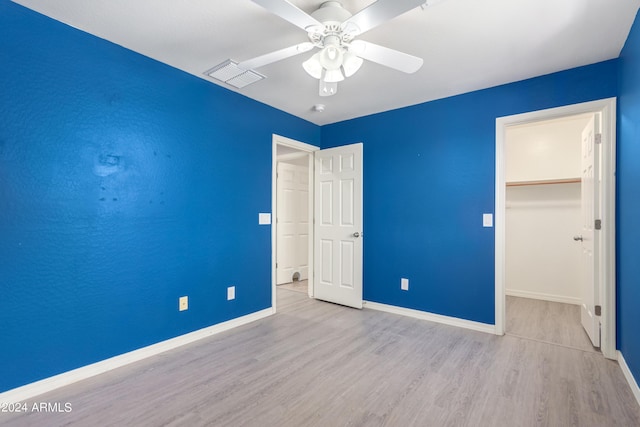 unfurnished bedroom featuring ceiling fan, light hardwood / wood-style flooring, a closet, and a walk in closet