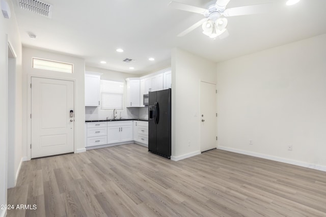 kitchen with sink, black fridge, white cabinetry, light hardwood / wood-style flooring, and ceiling fan