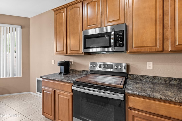 kitchen with appliances with stainless steel finishes, dark stone counters, and light tile patterned floors