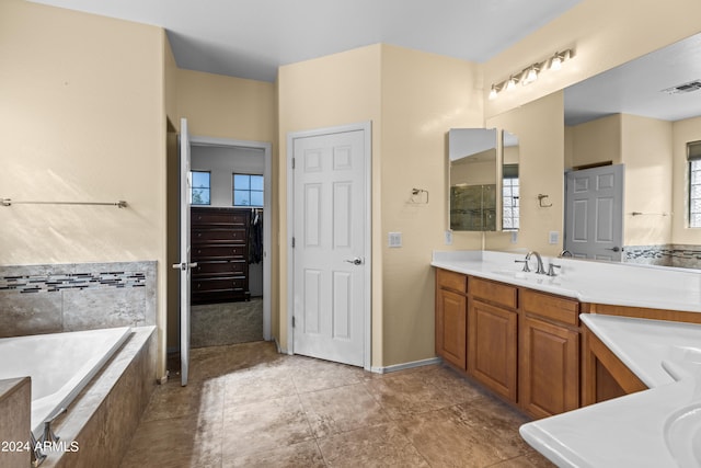 bathroom featuring a relaxing tiled tub, vanity, and a healthy amount of sunlight