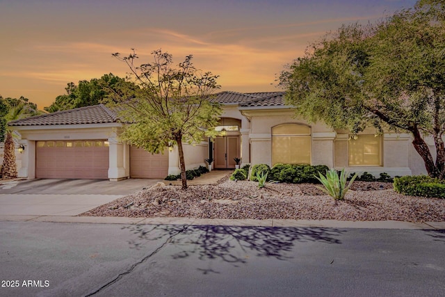 mediterranean / spanish home featuring stucco siding, driveway, an attached garage, and a tiled roof