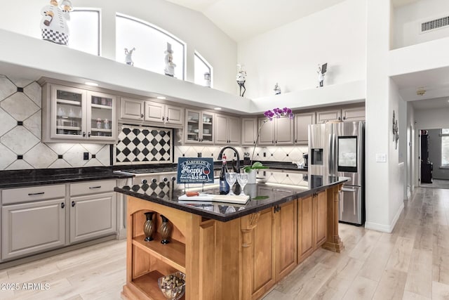 kitchen with visible vents, high vaulted ceiling, a center island with sink, appliances with stainless steel finishes, and glass insert cabinets