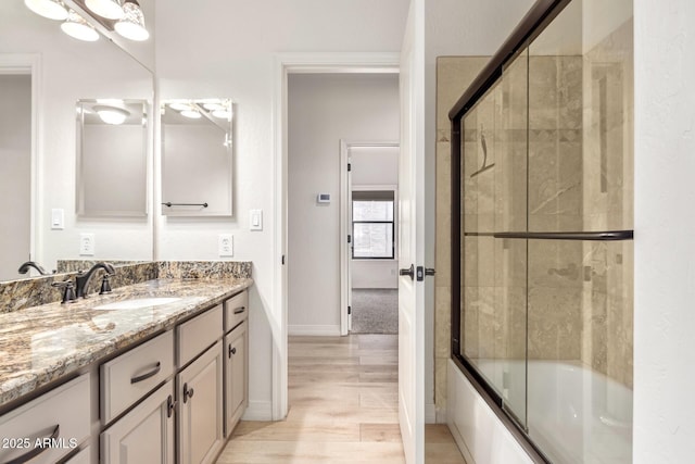 full bath with baseboards, bath / shower combo with glass door, wood finished floors, and vanity