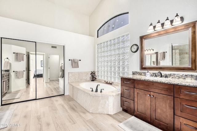 bathroom with vanity, a high ceiling, a bath, and wood finished floors