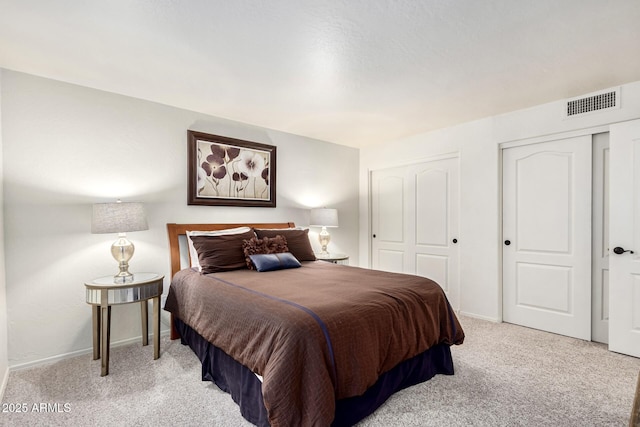 bedroom featuring baseboards, visible vents, multiple closets, and light carpet