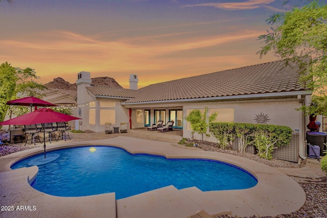 pool at dusk featuring cooling unit, an outdoor pool, and a patio