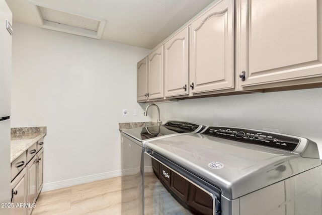 washroom with baseboards, attic access, light wood-style flooring, cabinet space, and washing machine and dryer