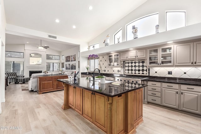 kitchen with visible vents, glass insert cabinets, ceiling fan, a center island with sink, and a sink