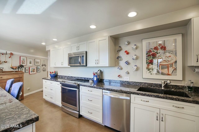 kitchen featuring stainless steel appliances, recessed lighting, white cabinets, a sink, and dark stone countertops