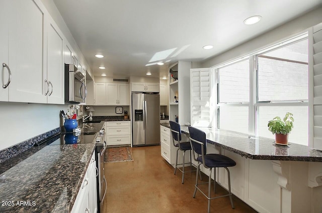 kitchen featuring a breakfast bar area, recessed lighting, white cabinets, appliances with stainless steel finishes, and dark stone counters