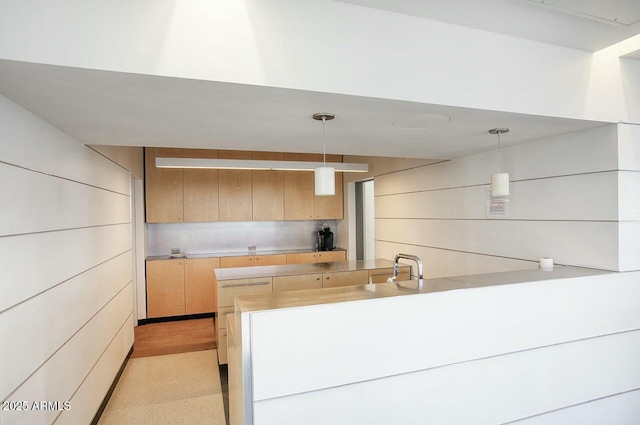 kitchen featuring a peninsula, light countertops, light brown cabinetry, pendant lighting, and a sink