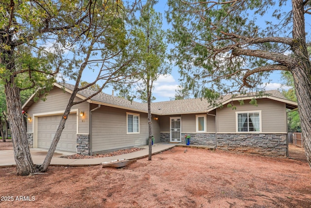 single story home with stone siding, an attached garage, a shingled roof, and driveway