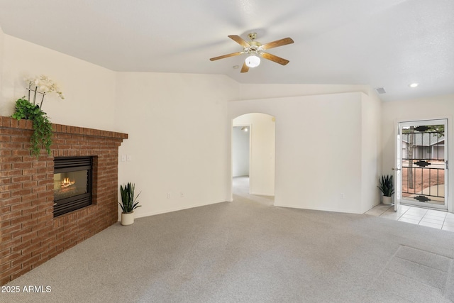 unfurnished living room with a fireplace, arched walkways, ceiling fan, vaulted ceiling, and light carpet